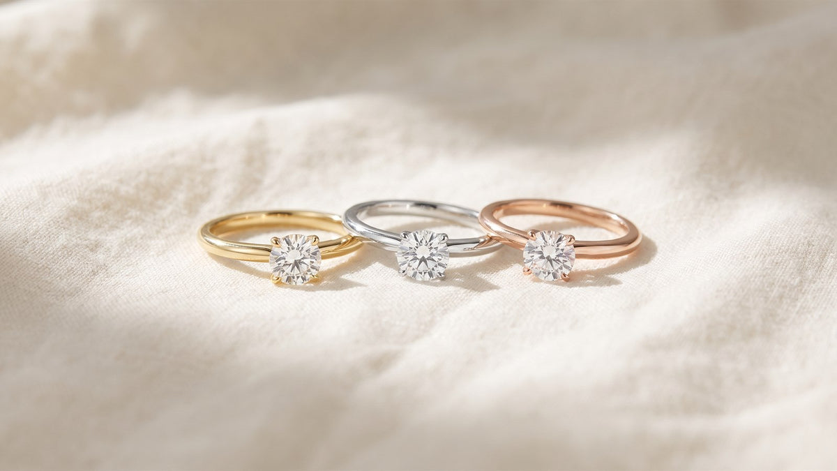 Three diamond solitaire rings in yellow, white and rose gold resting on cream linen