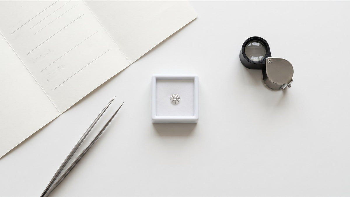 A loose round diamond in a gem box with tweezers, a loupe and report